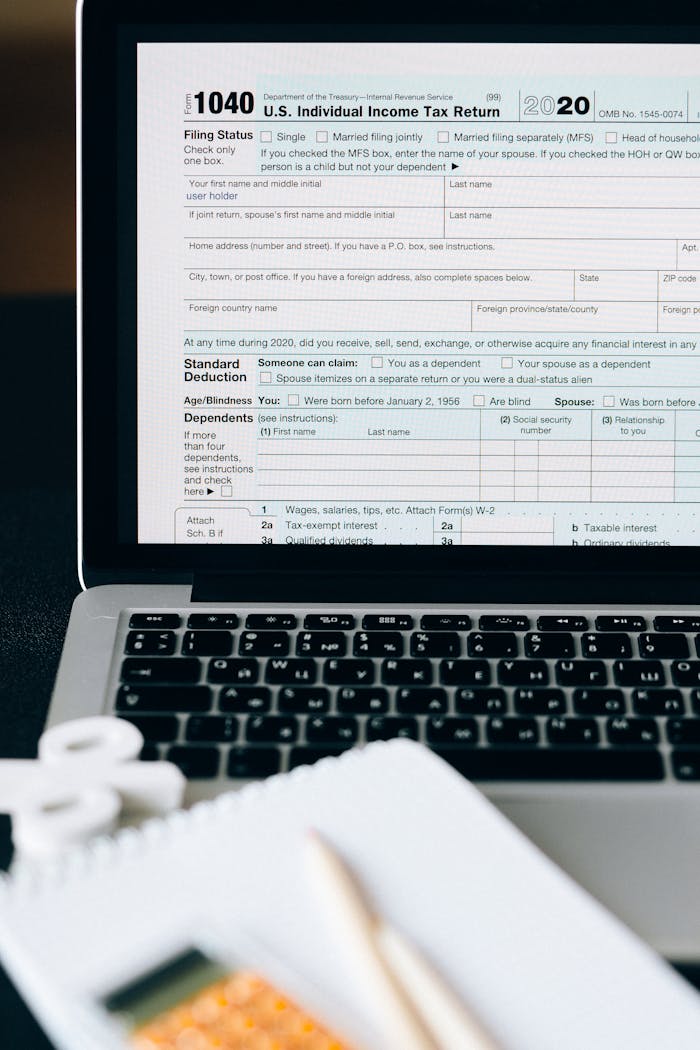 Home Close-up of a tax form on a laptop screen with a calculator and notebook in the foreground.