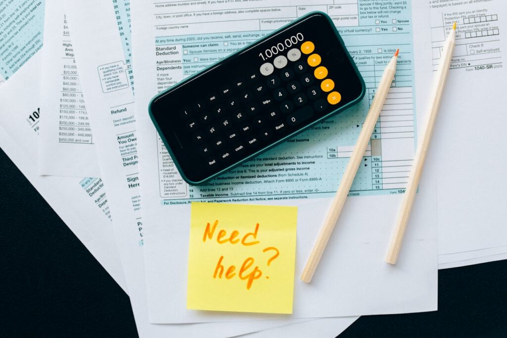 pexels photo 6863260 1 Top view of financial papers with a calculator, pencils, and a note saying 'Need help?' indicating tax or accounting assistance.